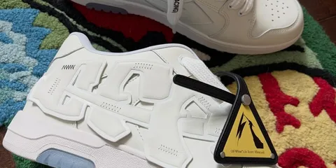 Chaussures blanches avec détails 3D et étiquette d'avertissement jaune.