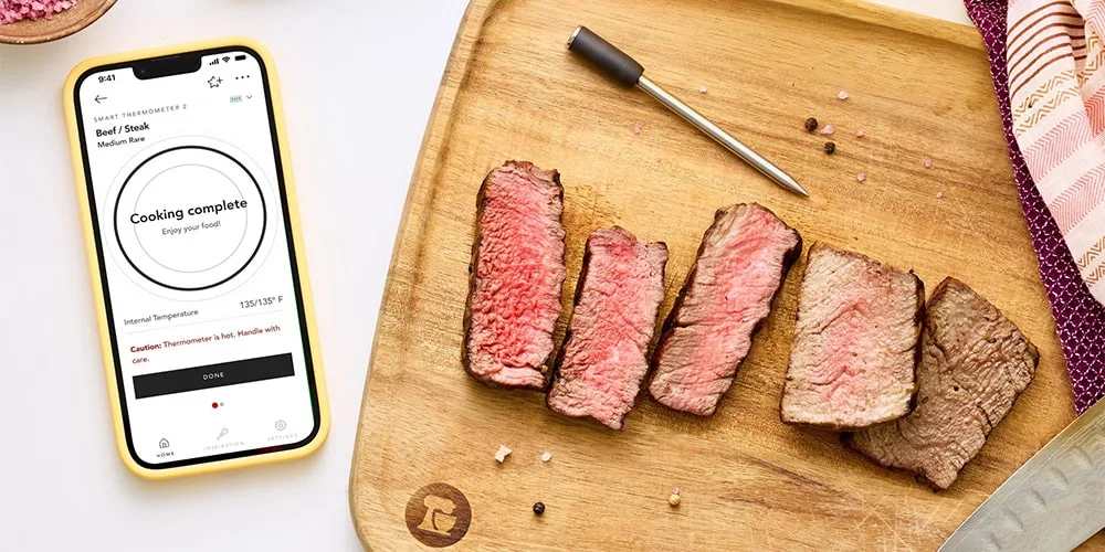 Planche avec viande cuite et thermomètre connecté affiché sur smartphone.