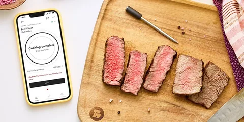 Planche avec viande cuite et thermomètre connecté affiché sur smartphone.