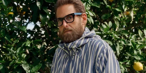 Homme barbu avec des lunettes devant des arbres.