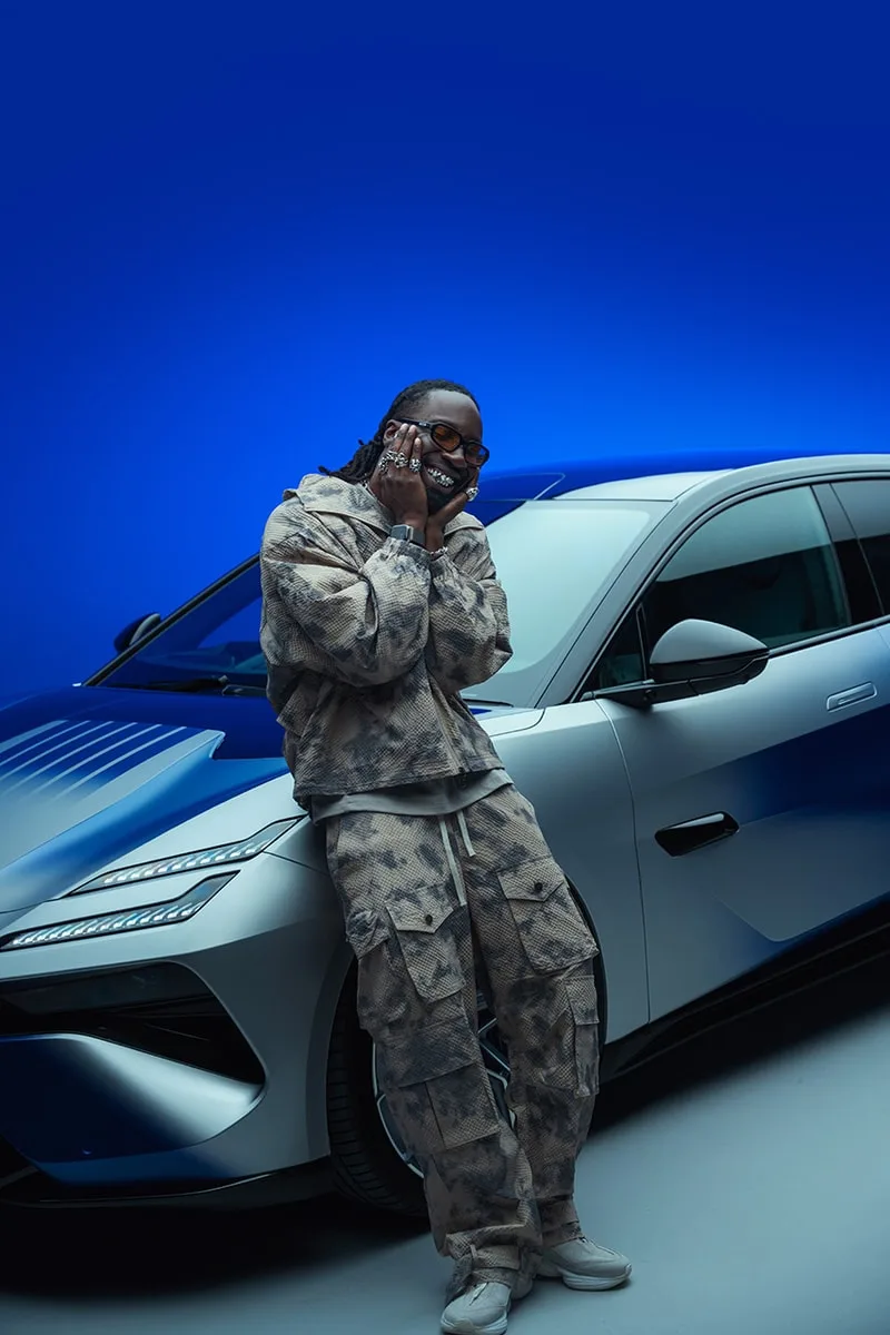 Personne posant devant une voiture bleue dans un studio illuminé.