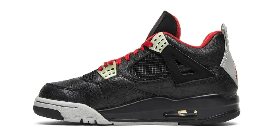 Chaussure noire avec détails rouges et filet noir, semelle grise et noire.