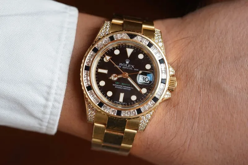 Montre Rolex en or avec diamants et cadran noir, portée au poignet.