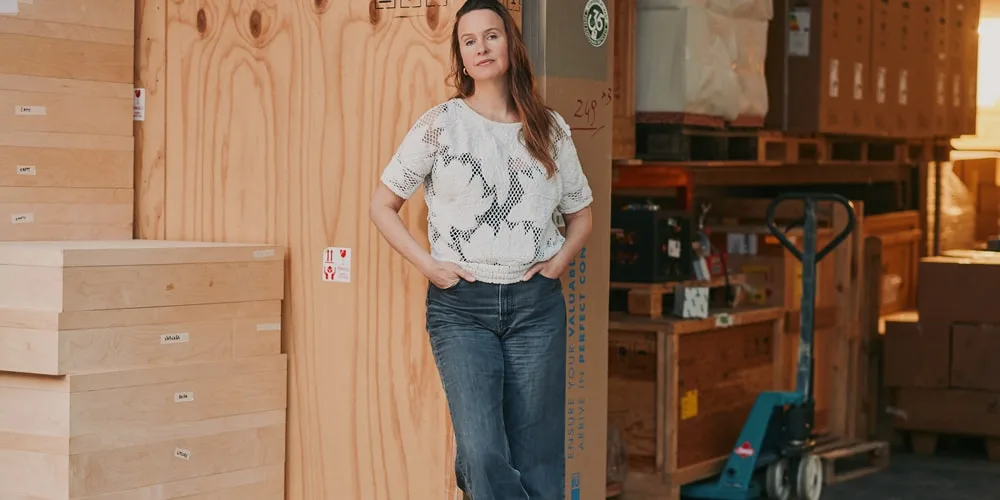 Femme debout dans un entrepôt avec boîtes et palettes.