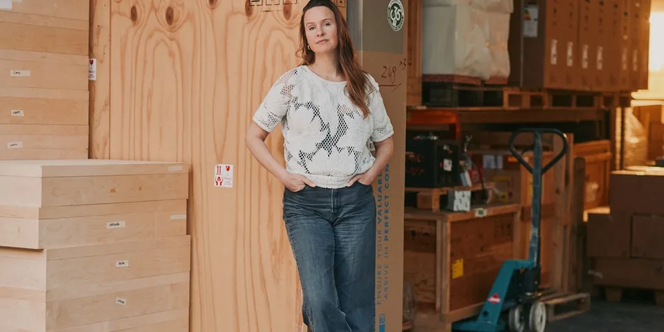 Femme debout dans un entrepôt avec boîtes et palettes.