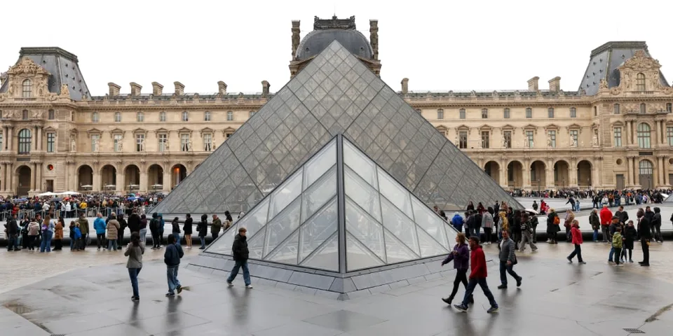 Pyramide du Louvre avec des visiteurs autour, bâtiment historique en arrière-plan.