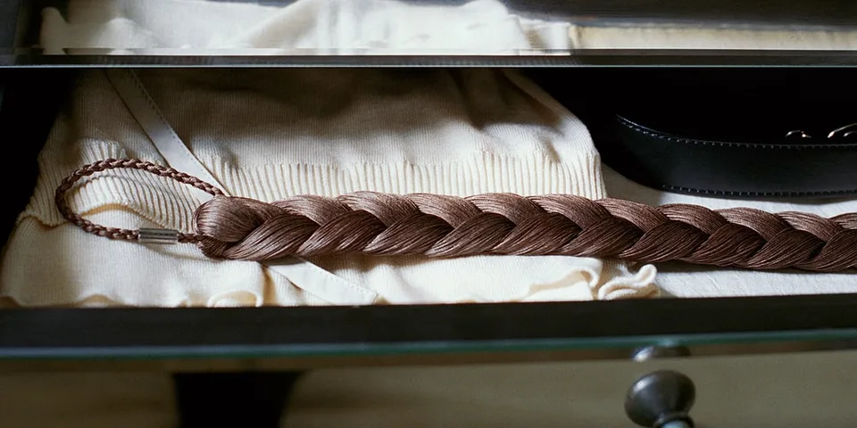 Tresse marron posée sur des vêtements dans un tiroir en verre.