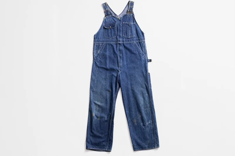 Salopette en denim bleu sur fond blanc.