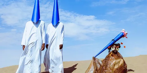 Personnes en robe blanche et masque conique bleu dans un désert sableux