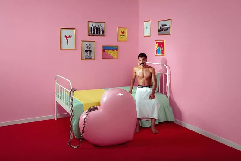 Homme assis sur un lit dans une chambre rose au décor éclectique.