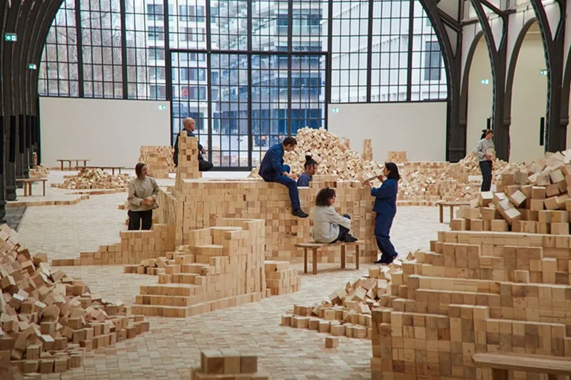 Installation artistique avec des blocs en bois et des personnes dans une salle.