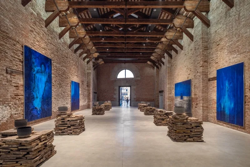 Grande salle avec tableaux bleus et sculptures sur piliers de pierre.