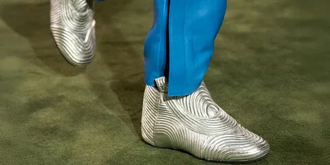 Chaussures argentées texturées avec pantalon bleu sur fond vert.
