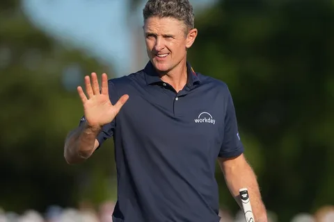 Homme saluant sur un parcours de golf, portant un polo bleu.