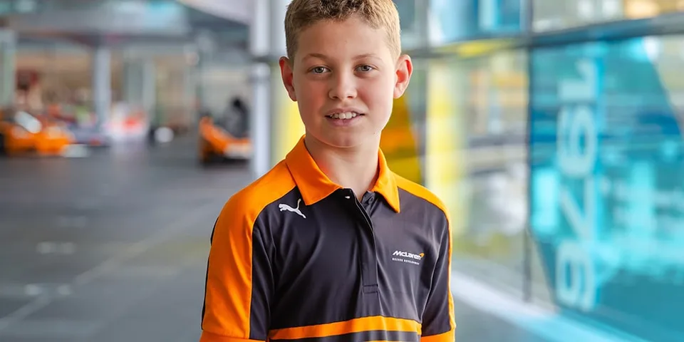 Jeune garçon portant un polo orange et noir souriant dans un hall moderne.
