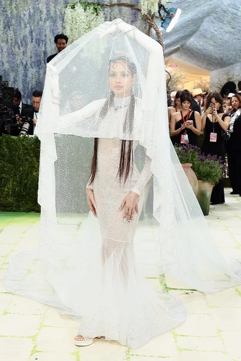 Femme en robe blanche élégante avec voile, entourée de photographes.