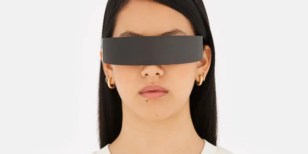 Personne avec des lunettes futuristes, cheveux longs et boucles d'oreilles en or.