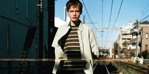 Personne devant une voie ferrée urbaine, portant une chemise à carreaux.