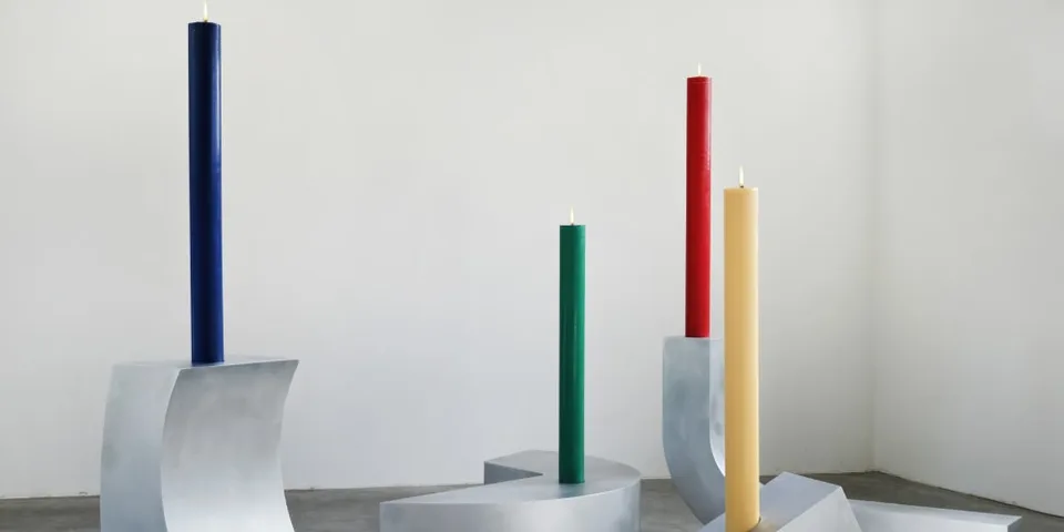 Bougies colorées sur des socles métalliques dans une galerie.