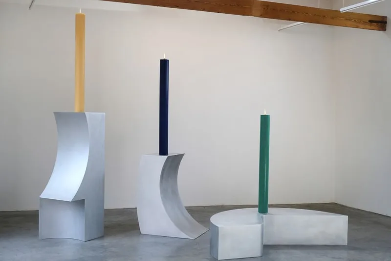 Trois bougies colorées sur des supports métalliques modernes dans une galerie.