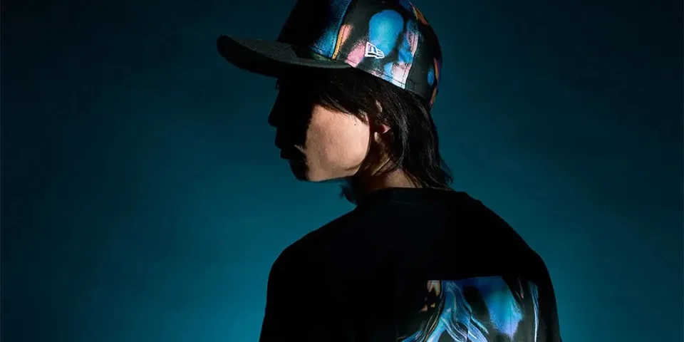 Personne portant une casquette et un t-shirt imprimé coloré, fond sombre.