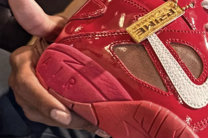 Main tenant une chaussure rouge brillante avec une étiquette dorée et le mot 'AIR' visible.