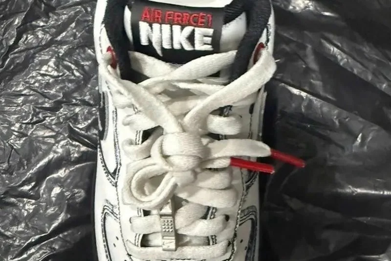 Chaussure Nike Air Force 1 blanche avec lacets et détails rouges sur fond noir.