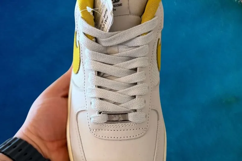 Main tenant une chaussure blanche et jaune avec lacets gris.