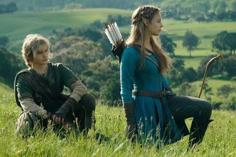 Deux personnages médiévaux dans une prairie verdoyante, avec arcs et flèches.