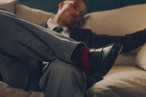 Personne assise sur un canapé en jean, chaussures noires et chaussettes rouges.