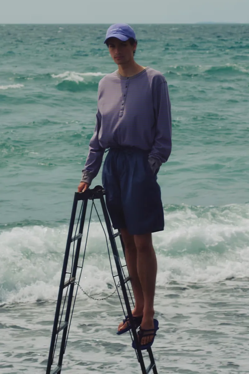 Un homme debout sur une structure métallique à la plage, vêtement décontracté.