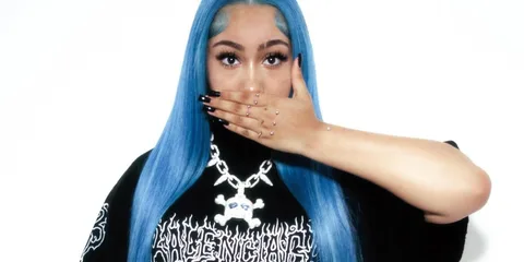 Femme aux cheveux bleus couvrant sa bouche avec une main ornée de bijoux.