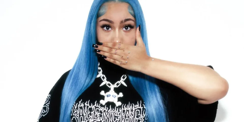 Femme aux cheveux bleus couvrant sa bouche avec une main ornée de bijoux.