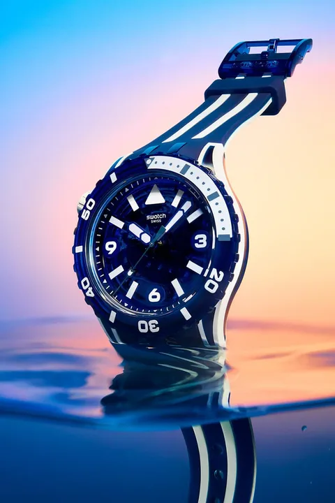 Montre de plongée posée sur l'eau avec fond coloré au coucher du soleil.