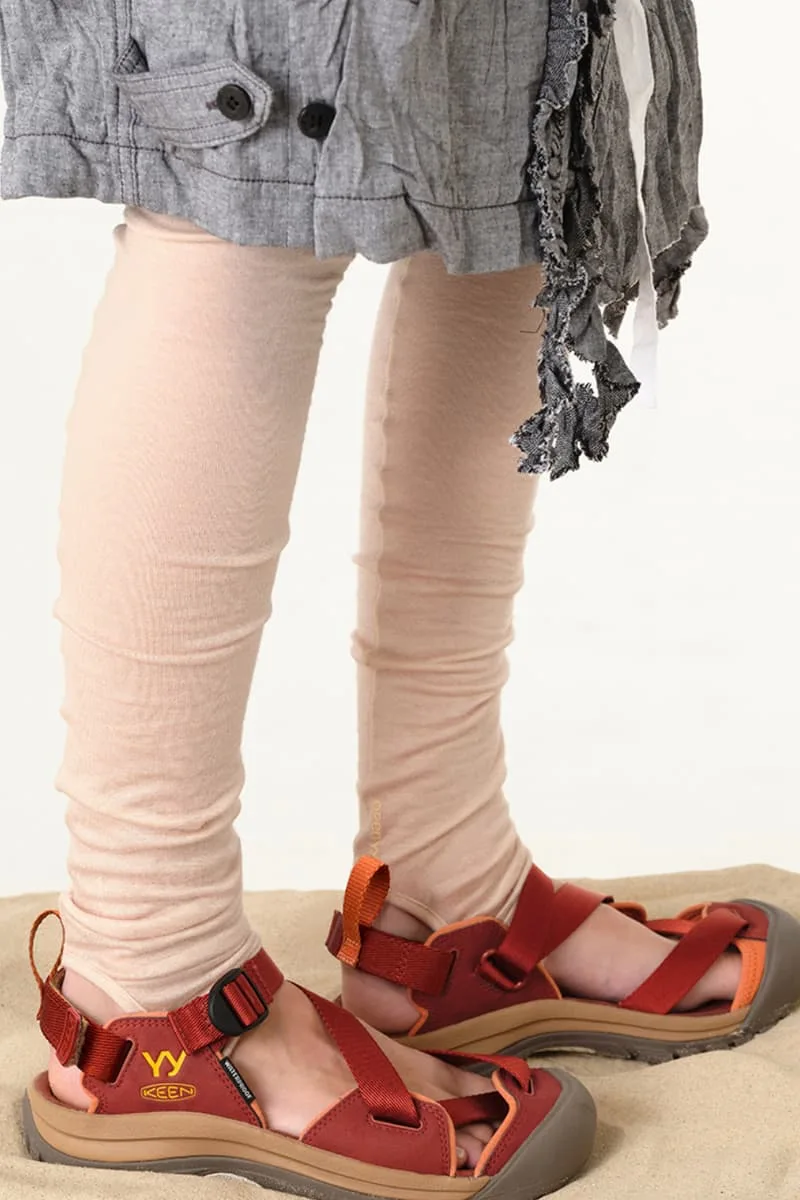 Personne portant des sandales rouges et un pantalon beige sur du sable.
