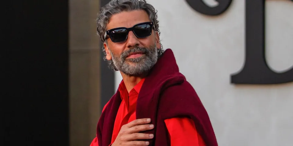 Homme avec lunettes de soleil et veste rouge, posant confiant.