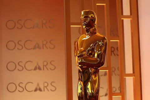 Statue dorée des Oscars devant le mot 'Oscars' sur fond orange.