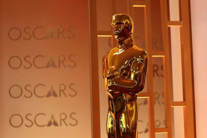 Statue dorée des Oscars devant le mot 'Oscars' sur fond orange.