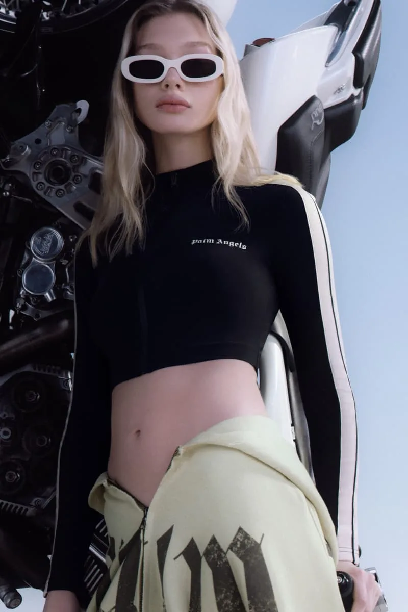 Femme en tenue de sport noire avec lunettes blanches, moto en arrière-plan.
