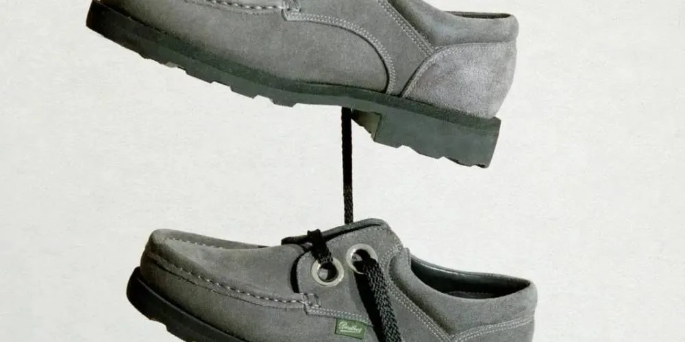 Deux chaussures grises en apesanteur, reliées par un lacet noir.