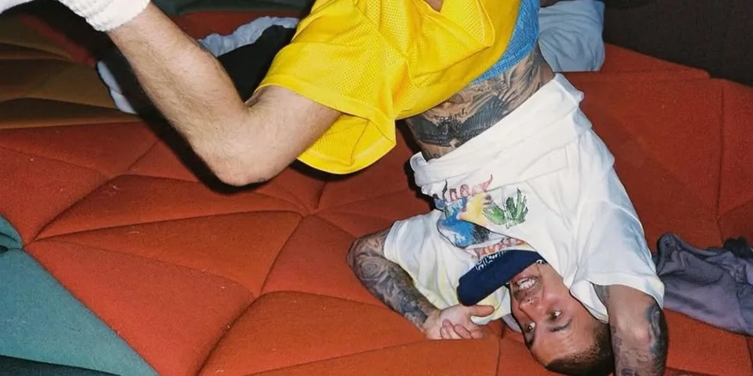 Homme en t-shirt blanc et short jaune, posé à l'envers sur un coussin coloré.