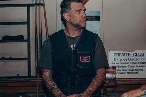 Homme tatoué en gilet en jean, dans un club privé.