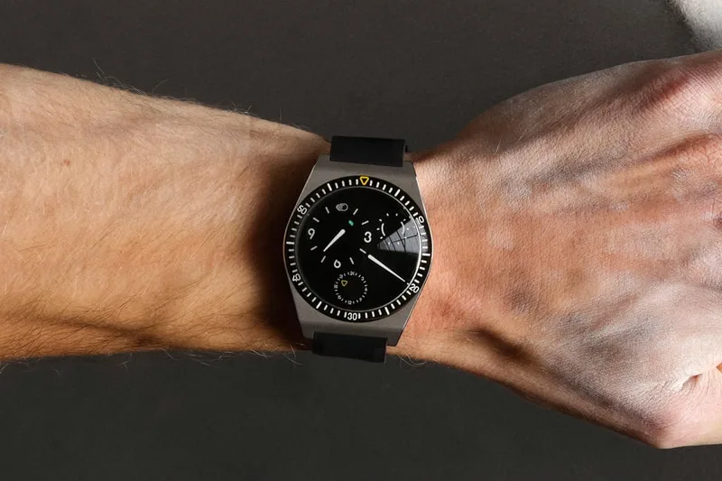 Montre avec cadran noir et bracelet noir sur un poignet.