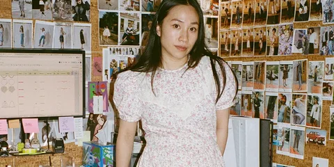 Femme en robe à fleurs, bureau avec photos au mur et écran d'ordinateur