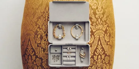 Boîte à bijoux ouverte avec bracelets et boucles d'oreilles sur fond orné.