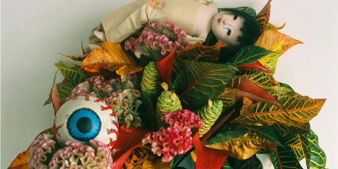 Poupée avec œil géant et feuilles colorées, arrangement créatif.
