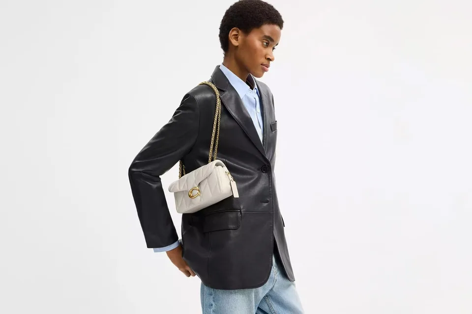 Personne portant un blazer noir et un sac blanc.