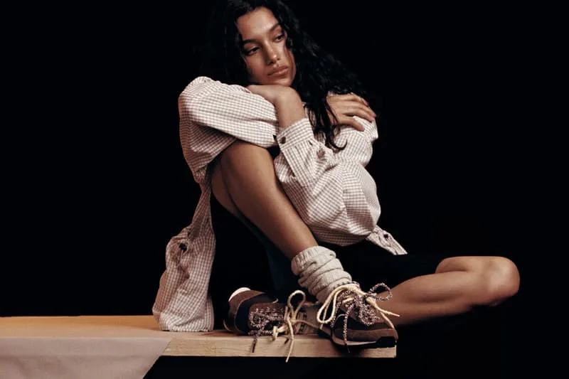 Personne assise avec une chemise à carreaux et des baskets sur fond noir.