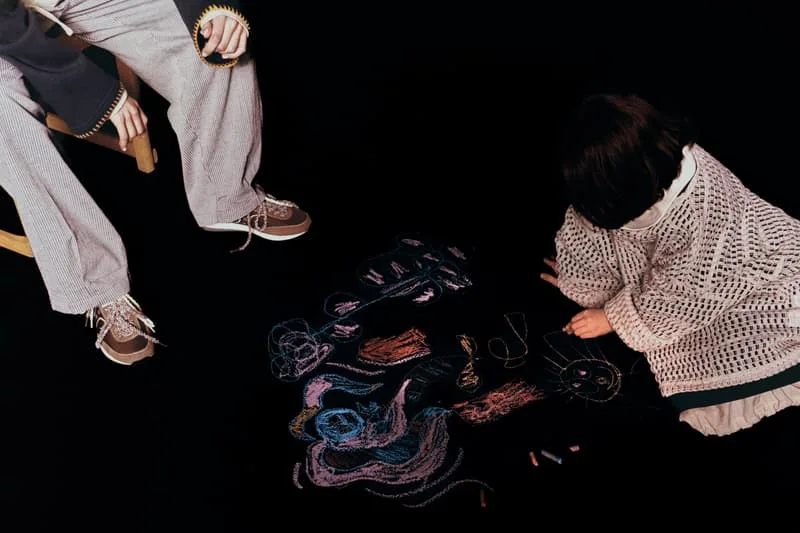 Deux personnes dessinent avec des craies colorées sur un sol sombre.