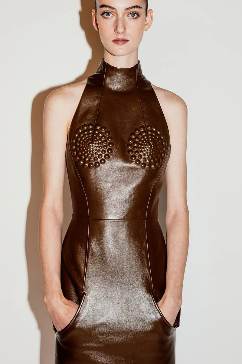 Personne en robe marron texturée avec les mains dans les poches.